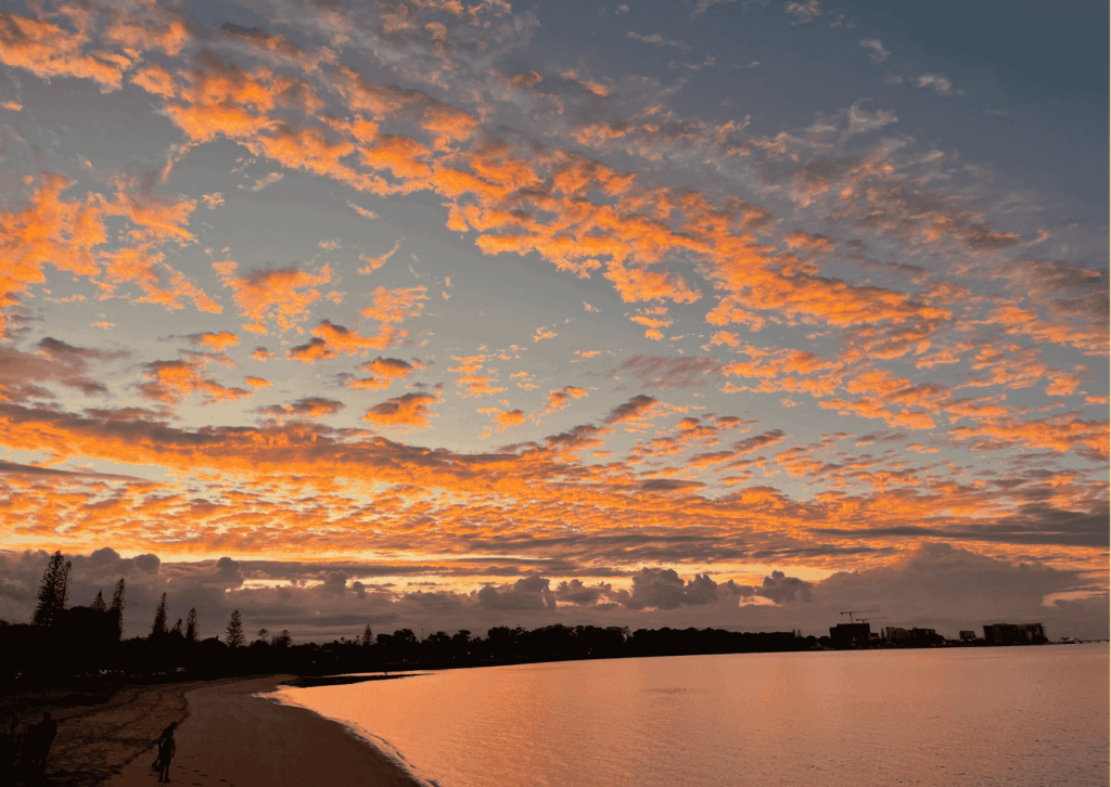 Orange clouds reflected over still bay water.